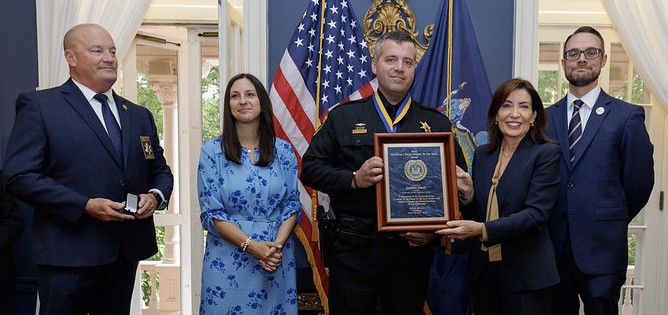 Governor Kathy Hochul presents the Governor’s Police Officer of the Year Award to Cortland County Sheriff’s Captain Anthony Phelps. Pictured above from left are Cortland County Sheriff Mark Helms; Captain Phelps’s wife Lauren; Captain Phelps; Governor Hochul and Joe Popcun, Executive Deputy Commissioner for the New York State Department of Criminal Justice Services.